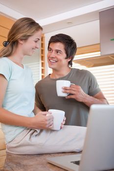 Portrait of a young couple having coffee while using a notebook in their kitchen