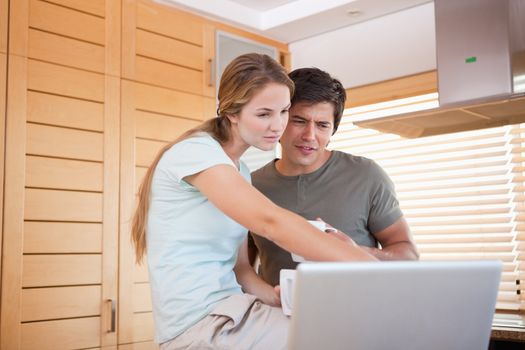 Young couple having tea while using a laptop in their kitchen
