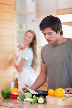 Portrait of a man cooking while his wife is washing the dishes in their kitchen