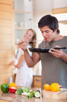 Portrait of a man cooking while his girlfriend is washing the dishes in their kitchen
