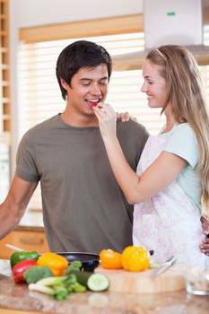 Portrait of a woman making her fiance tasting her meal while wearing an apron