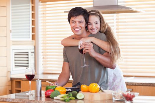 Lovely couple drinking red wine while hugging in their kitchen