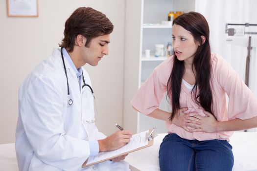 Young male doctor writing down female patients symptoms