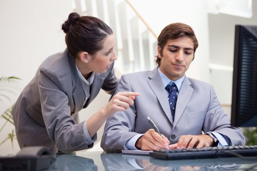Young businessman taking notes while getting explanation by colleague
