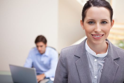 Smiling young businesswoman with colleague working on his laptop behind her