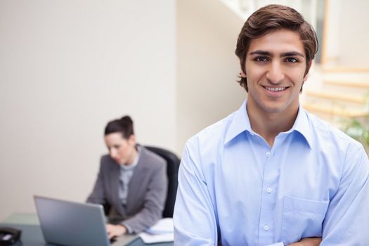 Smiling young businessman with colleague on her laptop behind him