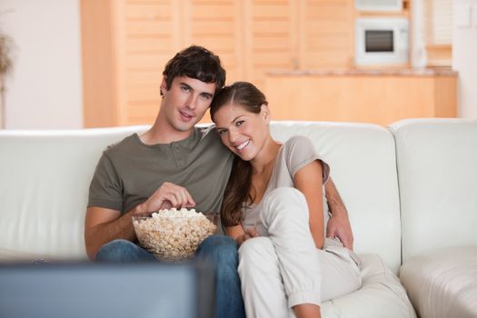 Young couple with bowl on popcorn watching a movie on the sofa