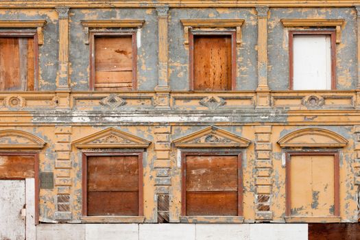 External facade with peeling paint of old boarded up abandoned derelict building with doors and window openings sealed with timber