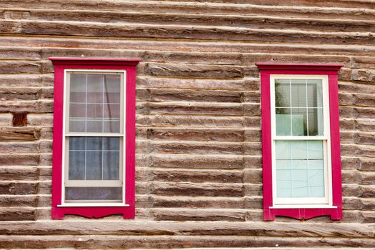 Architectural background of sash windows with colourful red frames in exterior facade of a log building