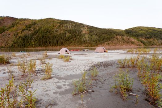 Beached canoes and two tents pitched on a sand bar alongside Yukon River, Yukon Territory, Canada, in remote boreal forest wilderness