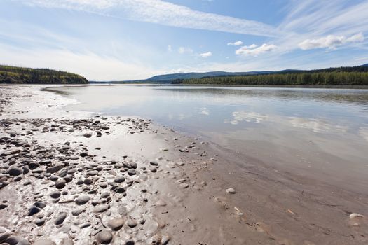 Gravel and mud at river bank of mighty stream Yukon River, Yukon Territory, Canada, near Dawson City forming a beautiful northern riverscape.
