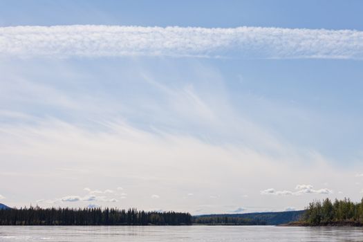 Some summer clouds in blue sky over mighty stream Yukon River, Yukon Territory, Canada, near Dawson City forming a beautiful northern riverscape.