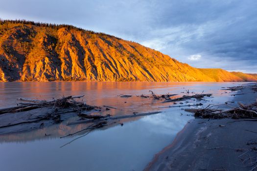 Eroded clay cliff river bank at Yukon River, Yukon Territory, Canada, near Dawson City glowing in orange light of summer sunset sun