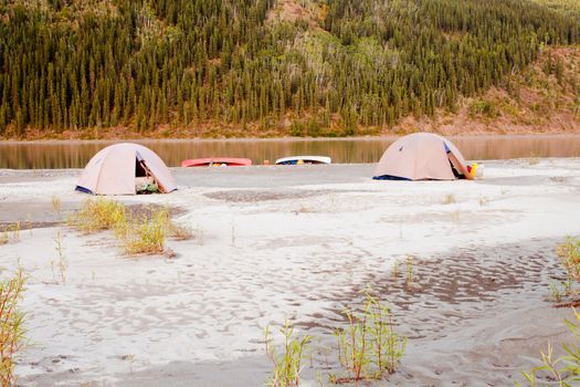 Beached canoes and two tents pitched on a sand bar alongside Yukon River, Yukon Territory, Canada, in remote boreal forest wilderness
