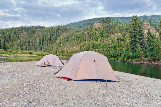 Two tents pitched on a sand bar alongside McQuesten River, Yukon Territory, Canada, in remote boreal forest wilderness
