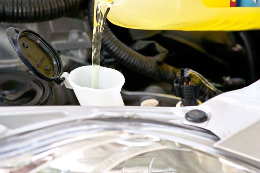A container of a yellow liquid is filling a container with engine parts in the background