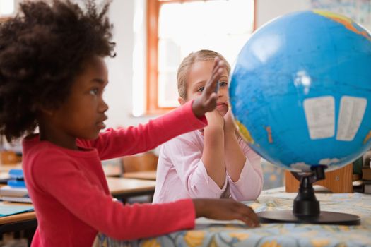 Happy schoolgirls looking at a globe in a classroom