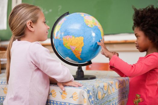 Smiling schoolgirls looking at a globe in a classroom
