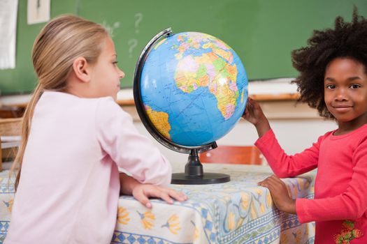 Cute schoolgirls looking at a globe in a classroom