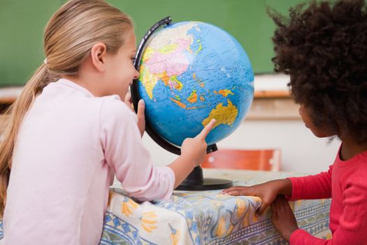 Little schoolgirls looking at a globe in a classroom