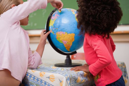 Schoolgirls pointing at a country on a globe