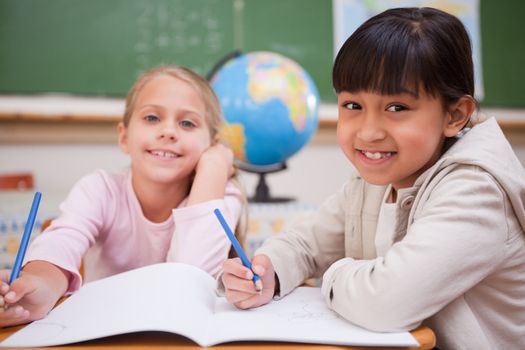 Smiling schoolgirls doing classwork while looking at the camera