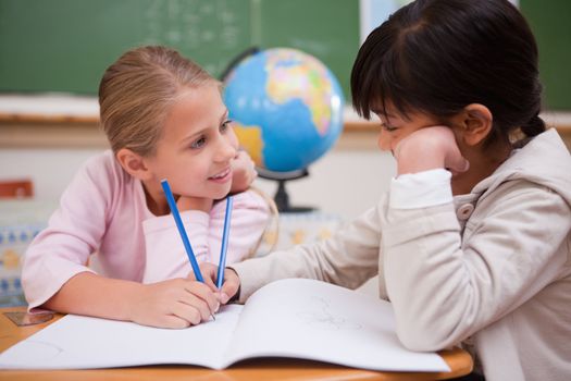 Cute schoolgirls doing classwork while looking at each other