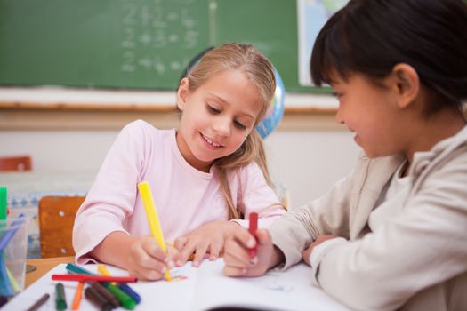 Smiling schoolgirls drawing in a classroom