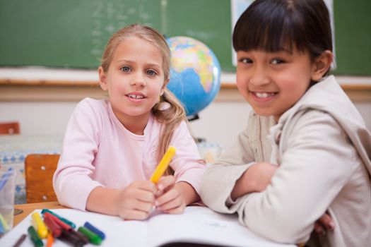 Schoolgirls drawing while looking at the camera in a classroom