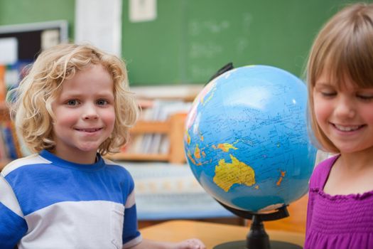 Young pupils posing in front of a globe in a classroom