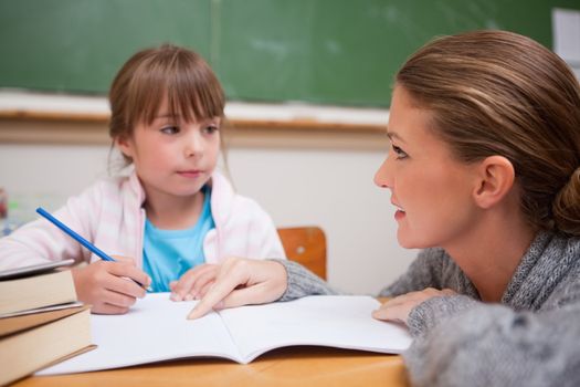 Schoolgirl writing a while her teacher is talking in a classroom