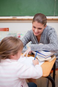 Portrait of a schoolgirl writing with her teacher in a classroom