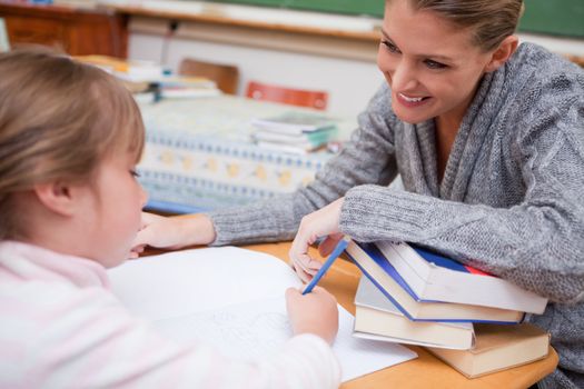 Schoolgirl writing with her smiling teacher in a classroom