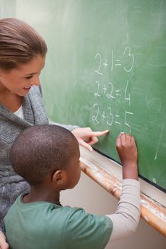 Portrait of a cute teacher and a pupil making an addition on a blackboard