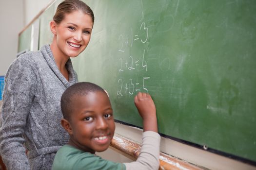 Smiling teacher and a pupil making an addition on a blackboard
