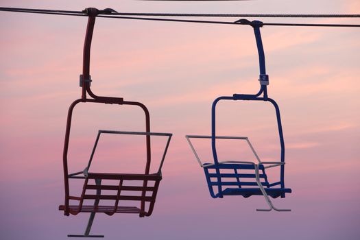 Red and blue empty seats of chair lift against red dawn sky; location is New Jersey shore, Seaside Heights, Casino Pier; 
