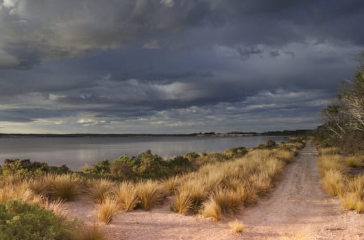 Sandy road along bay with cloud-filled sky as storm passes and sunlight breaks through.  Stokes Bay, Kangaroo Island, South Australia.