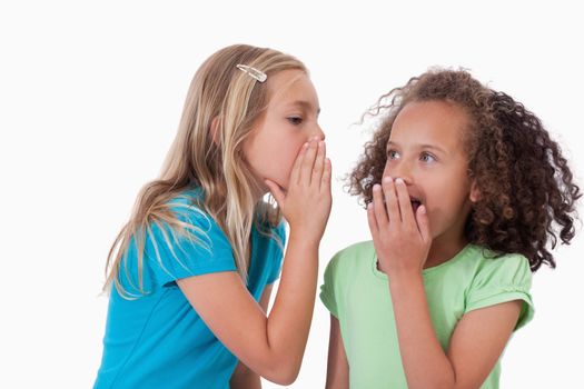 Cute girl whispering a secret to her friend against a white background