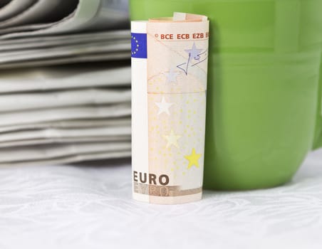 Euro currency with green mug placed in front of stack of newspapers; euro zone in the news; 