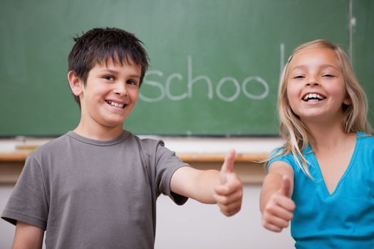 Happy pupils posing with the thumb up in a classroom