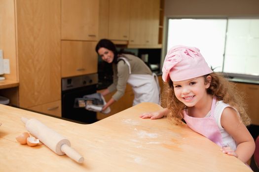 Young girl sitting in the kitchen while her mother puts cookies into the oven