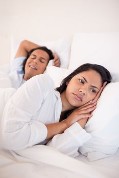 Displeased young woman lying next to snoring boyfriend