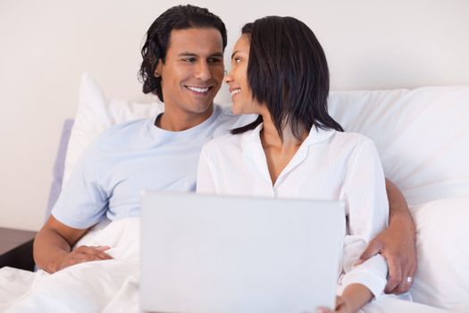 Smiling young couple sitting on the bed with their laptop