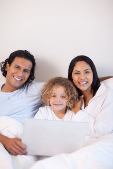 Young family sitting on the bed with notebook together