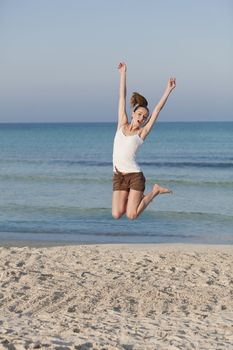 Girl young cheerful woman jumping in the air on the beach in the sand in the morning on the sea in summer vacation