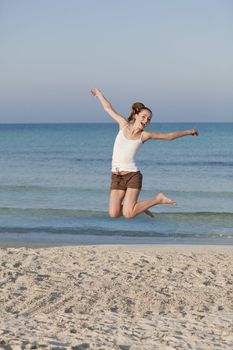 Girl young cheerful woman jumping in the air on the beach in the sand in the morning on the sea in summer vacation