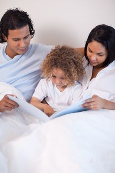 Young family sitting on the bed reading a story