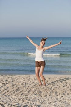 Girl young cheerful woman jumping in the air on the beach in the sand in the morning on the sea in summer vacation