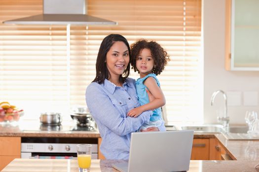 Young mother and daughter with notebook in the kitchen together