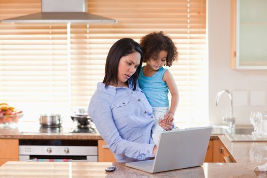 Young mother and daughter using laptop in the kitchen together